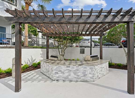 A wooden pergola is over a stone bench.