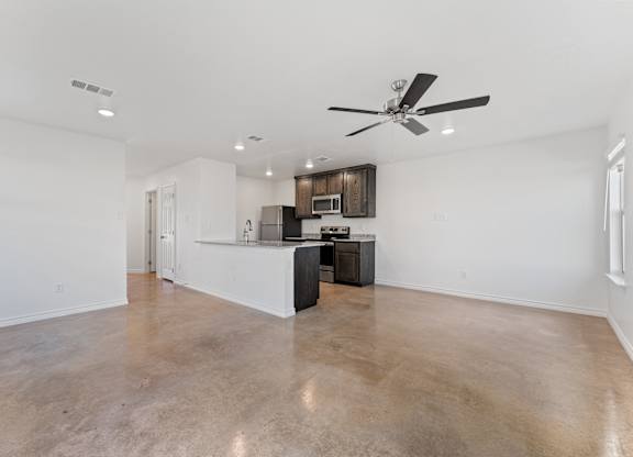 an empty living room with a kitchen and a ceiling fan