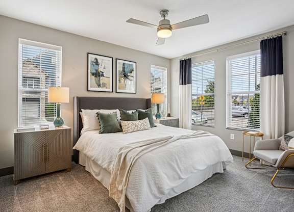 A bedroom with a large bed, a ceiling fan, and two lamps.