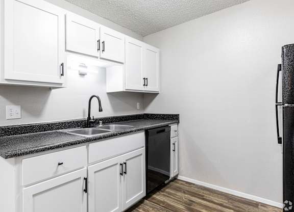 A kitchen with white cabinets and a black fridge.