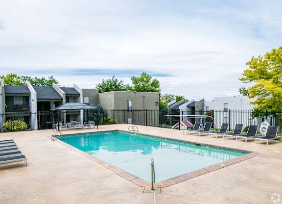 A swimming pool surrounded by a black fence and a few chairs.