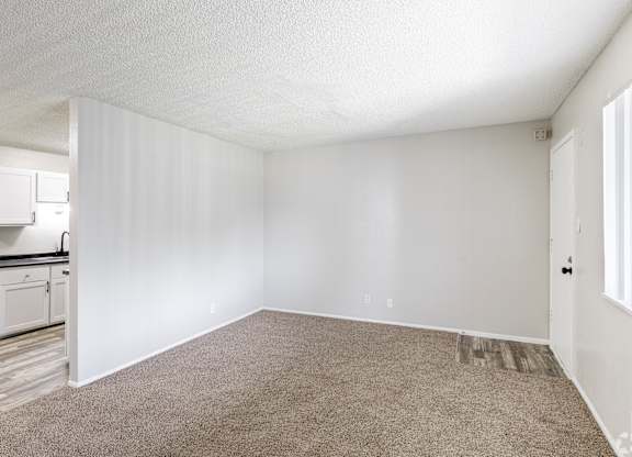 A small kitchen with white cabinets and a countertop is visible from an empty room.