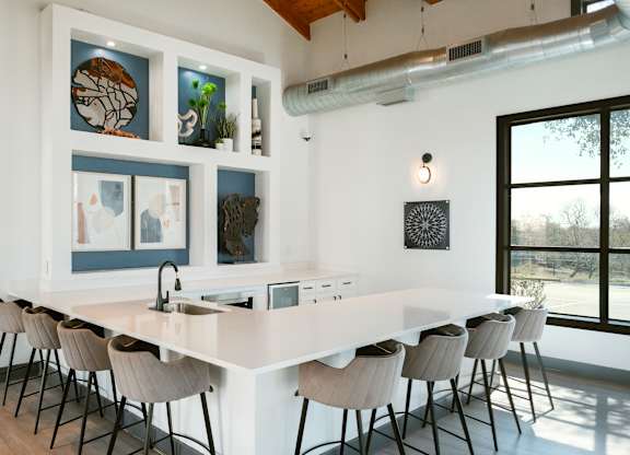 A kitchen with a long white island and chairs.