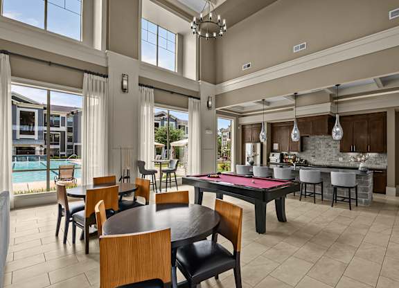 A modern dining room with a pool table and a kitchen in the background.