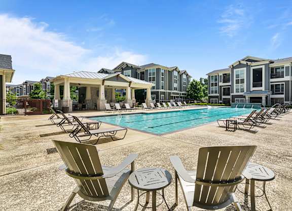 A pool surrounded by chairs and tables in front of apartment buildings.