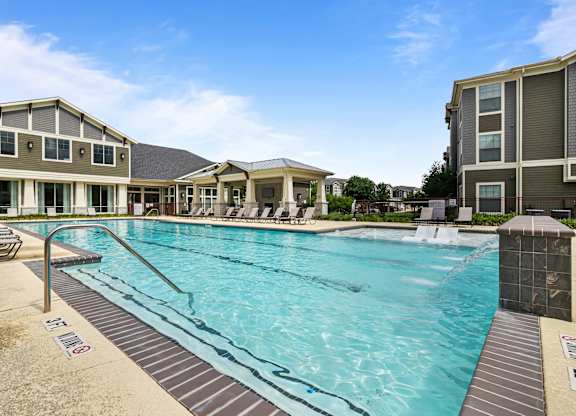 A large swimming pool in front of a building with a sunny sky.