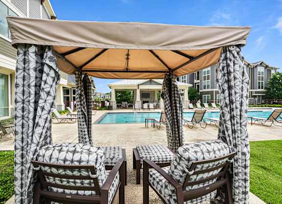 Two chairs are under a canopy by a pool.