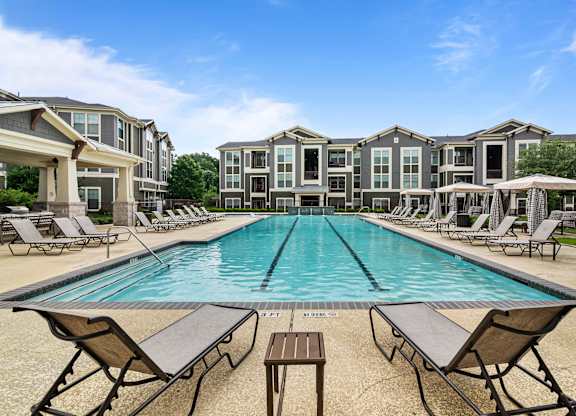 A large swimming pool surrounded by lounge chairs and apartment buildings.