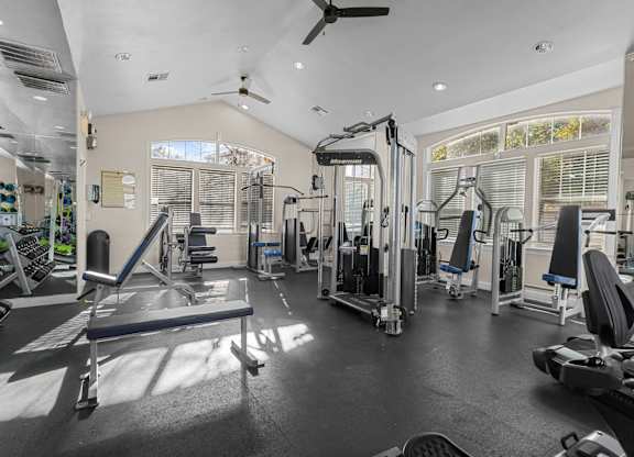 A spacious gym with a variety of equipment and a fan on the ceiling.