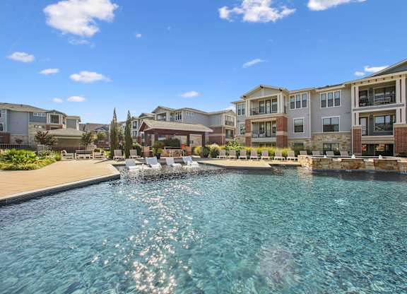A swimming pool in front of apartment buildings on a sunny day.