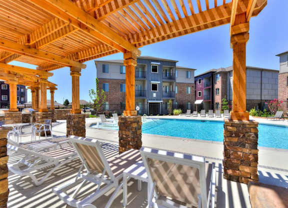 A wooden pergola over a pool with lounge chairs underneath.