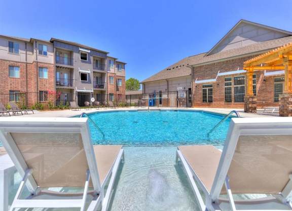A pool with a waterfall and two loungers in front of apartment buildings.