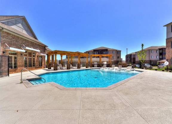 A large swimming pool surrounded by a concrete patio and a wooden pergola.