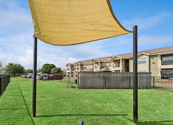A yellow shade sail over a green lawn in front of apartment buildings.