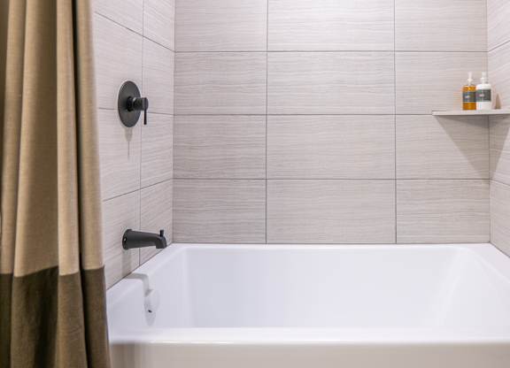 A white bathtub in a bathroom with beige tiles and a beige shower curtain.