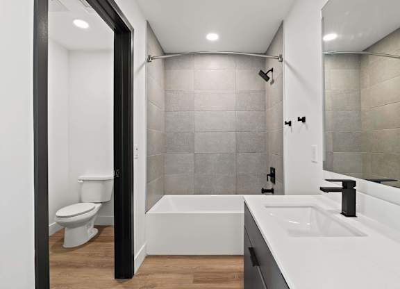 A modern bathroom with a white tub, sink, and tiled walls.