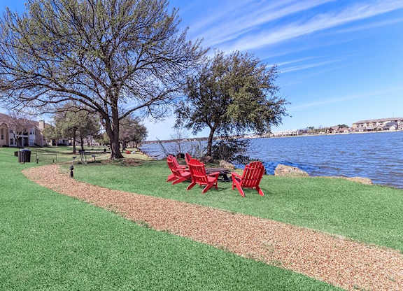 A lawn with a red chair and a table is in front of a body of water.