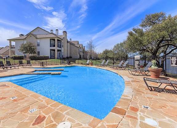 A large swimming pool surrounded by a stone patio and a house in the background.
