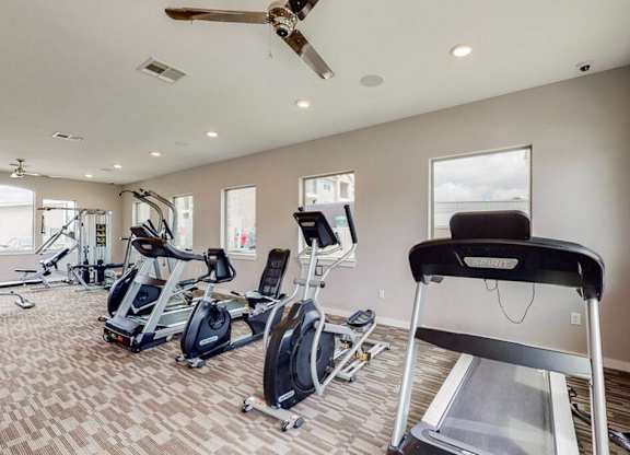 A home gym with a treadmill, elliptical machines, and a fan.