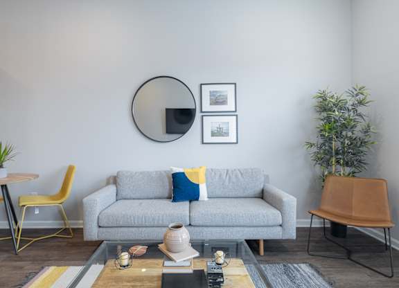 A living room with a grey couch, a yellow chair, a wooden table, and a plant.
