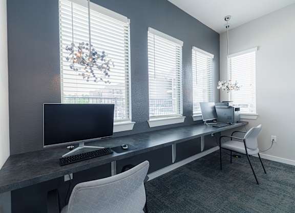 A modern home office with a black computer monitor and keyboard on a desk with a chair.