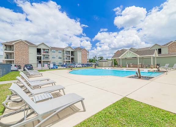 A swimming pool surrounded by lawn chairs and apartment buildings.