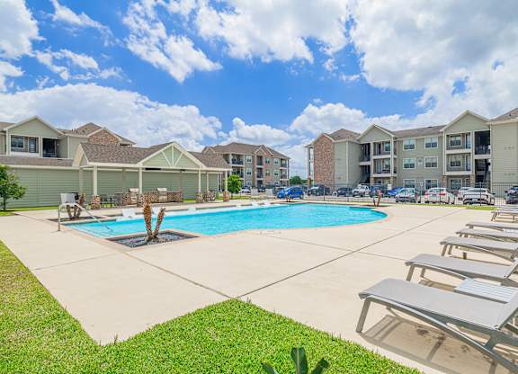 A swimming pool surrounded by lounge chairs in a residential area.