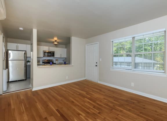 an empty living room with a kitchen in the background