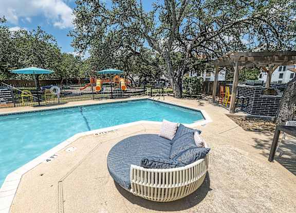 A round wicker lounge chair with a blue cushion sits on the edge of a pool.