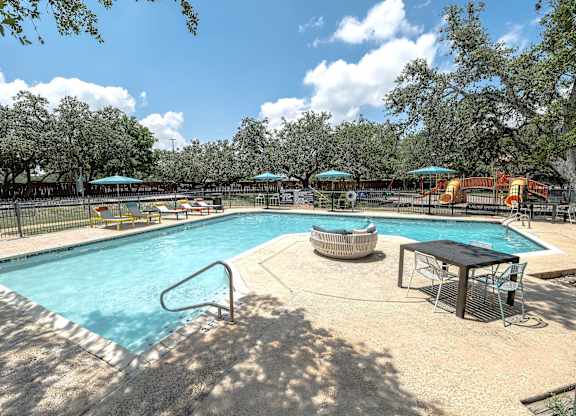 A large outdoor swimming pool surrounded by trees and a fence.