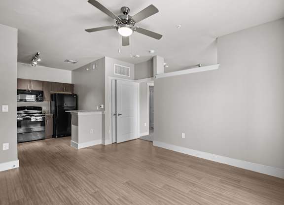 an empty living room with a ceiling fan and a kitchen