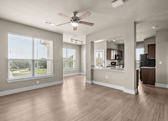 an empty living room with a ceiling fan and a kitchen