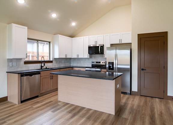 A modern kitchen with wooden floors and stainless steel appliances.