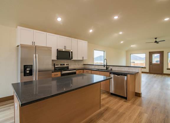 A kitchen with a black counter top and wooden floors.