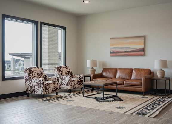 A living room with a brown leather couch, two patterned chairs, and a painting on the wall.