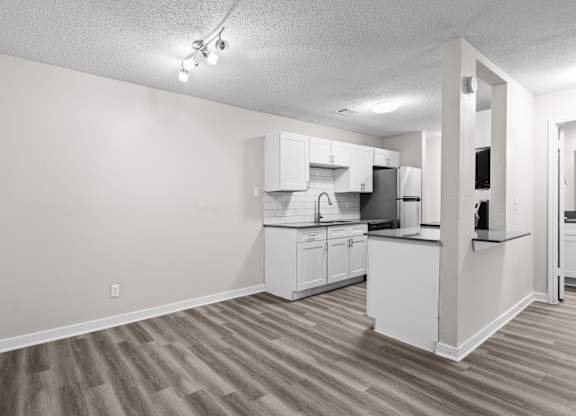 the living room and kitchen of an apartment with a wood floor and white cabinets