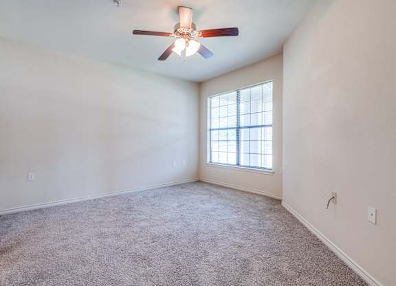 an empty living room with a ceiling fan and a window