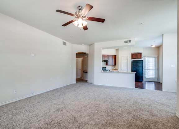 an empty living room with a ceiling fan and a kitchen