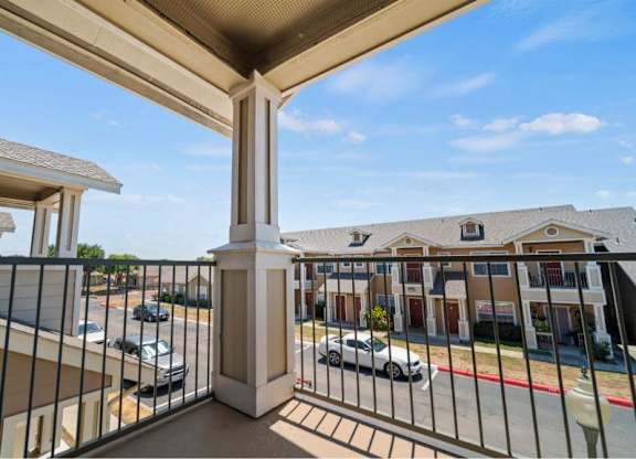 A balcony overlooks a parking lot and buildings.