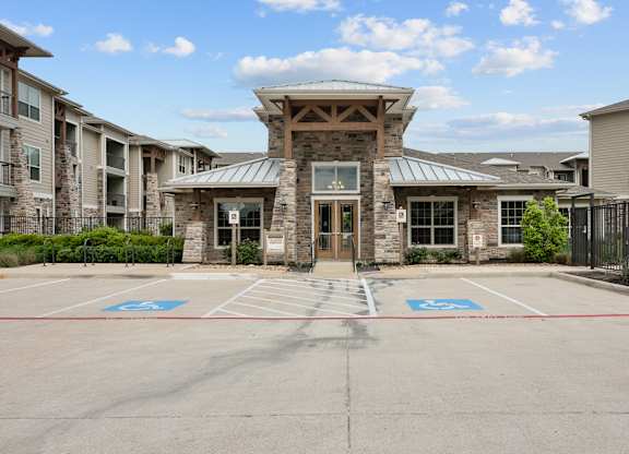A parking lot in front of a building with a stone facade and a covered entrance.