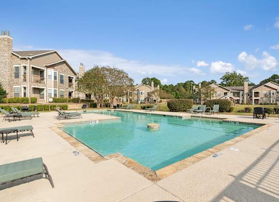 A large swimming pool surrounded by a concrete patio and lounge chairs.