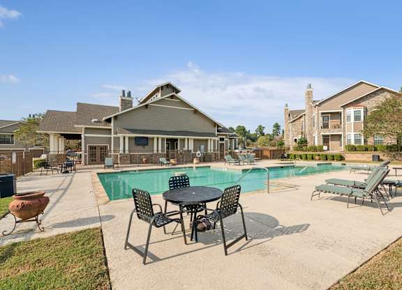 A pool area with a table and chairs in front of a building.
