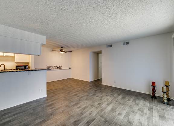 the living room and kitchen of an apartment with a hard wood floor and white walls