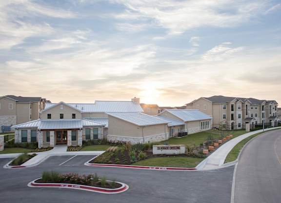 A sunset view of a building with a parking lot in front.