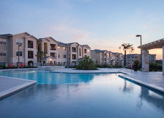 A swimming pool in front of apartment buildings at dusk.