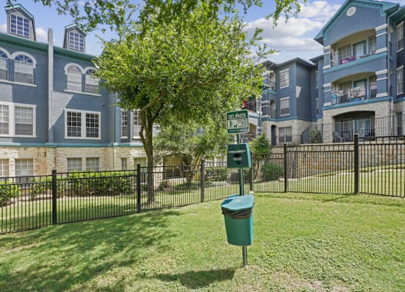 A tree in front of a building with a green trash can in front of it.
