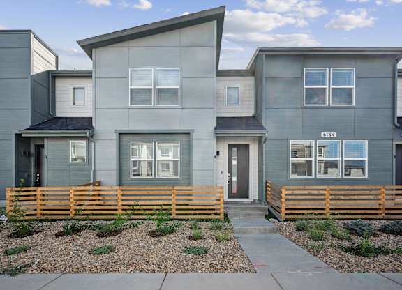 A modern house with a grey facade and a wooden fence in front.