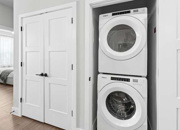 A white washing machine is stacked on top of a white dryer in a white cabinet.