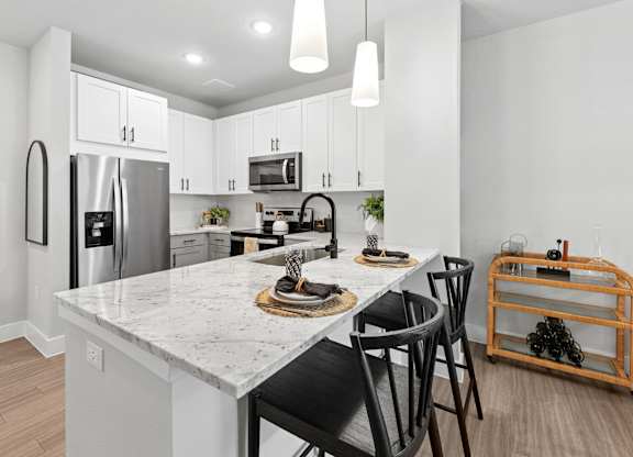A kitchen with a marble countertop and black chairs.