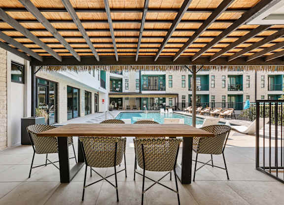 A table with chairs is set up outside with a pool and buildings in the background.